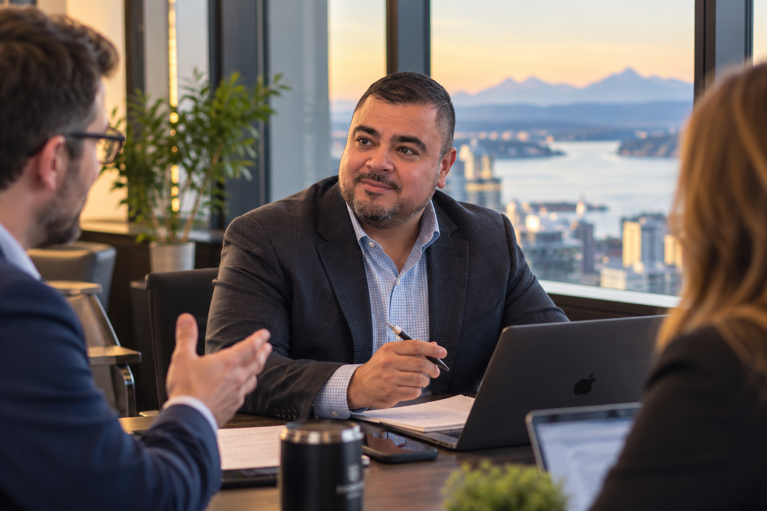 John Varela in a boardroom meeting with business leaders, overlooking the Seattle skyline at golden hour